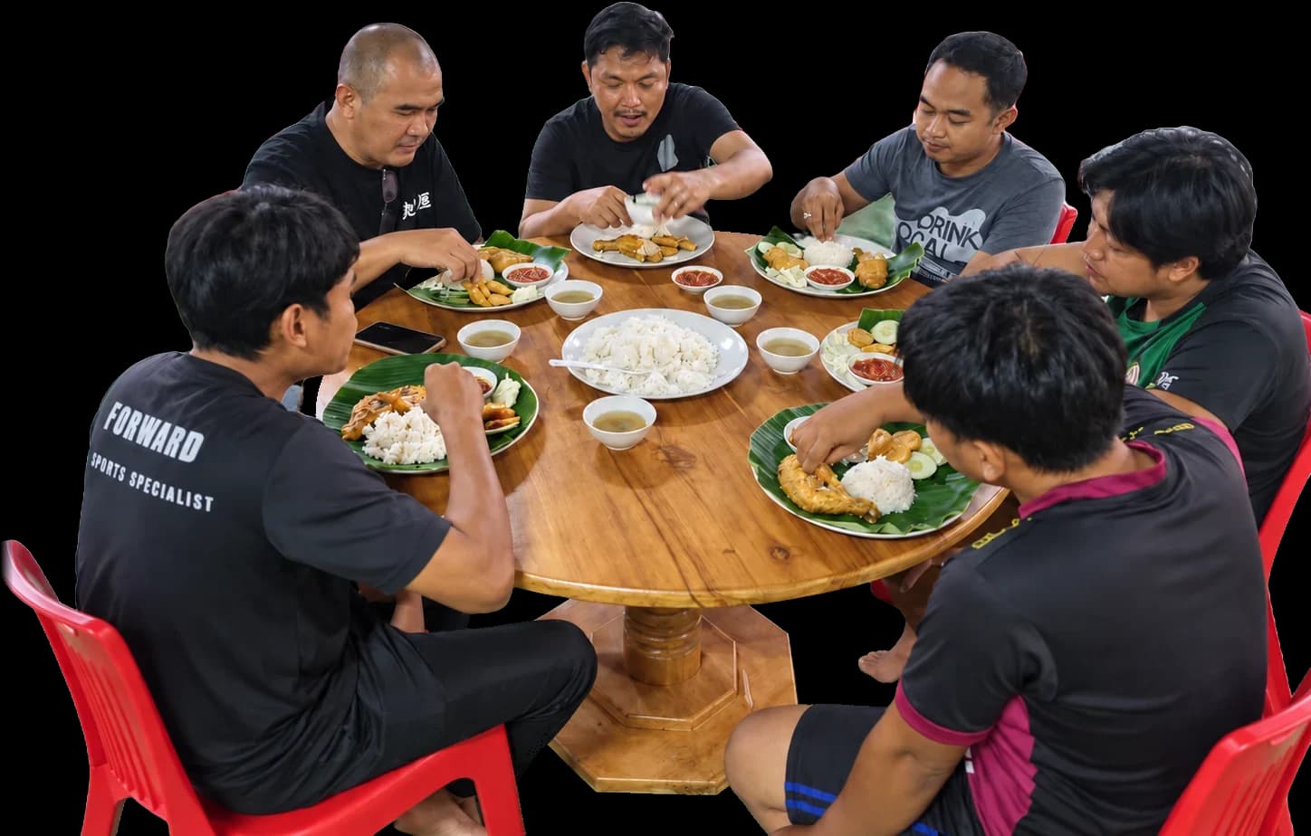 Seven people around a round wooden table at D’Cafe, every one of them with a plate of ayam penyet on a banana leaf, rice and soup in the middle